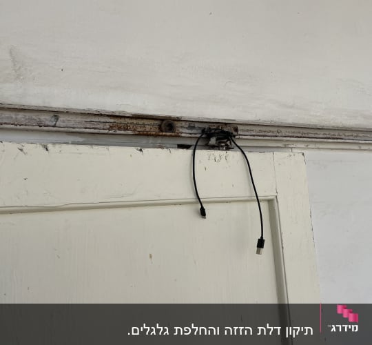 דלת עץ לבנה עם מסילה חלודה וכבל תלוי